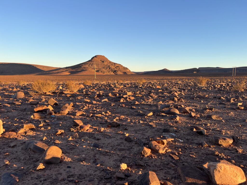 Rocky orange desert landscape, outside of Ourzazate, Morocco. Long shadows cast across the rocks, the sun is adding to the golden glow