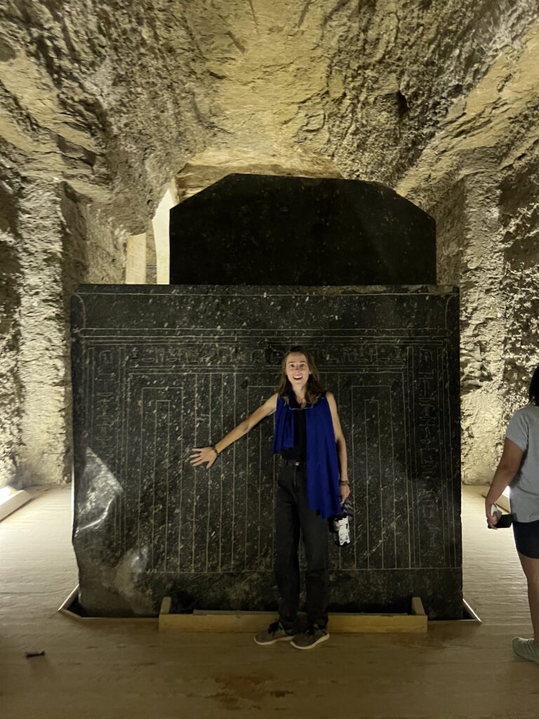 Bailey in front of a granite sarcophagus much bigger than her, with ancient Egyptian drawings inscribed on the side