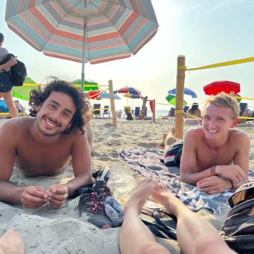 Two shirtless friends who met during sabbatical travel, one local and one foreigner, smiling at the beach in Lima, Peru
