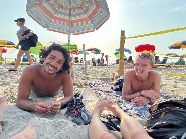 Two shirtless friends who met during sabbatical travel, one local and one foreigner, smiling at the beach in Lima, Peru