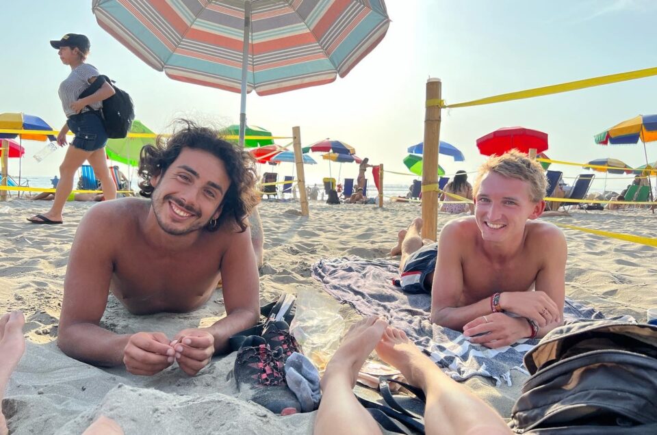 Two shirtless friends who met during sabbatical travel, one local and one foreigner, smiling at the beach in Lima, Peru